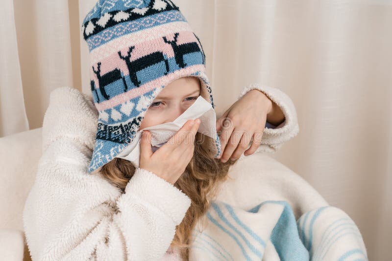 Kindermädchen zu Hause im Stuhl mit woolen umfassendem Niesen der warmen Strickmütze im Taschentuch Jahreszeitherbst-Winterkälten lizenzfreies stockbild Kindermädchen zu Hause im Stuhl mit woolen umfassendem Niesen der warmen Strickmütze im Taschentuch Jahreszeitherbst-Winterkälten lizenzfreies stockbild