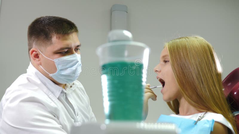 Kinderpatientin auf Zahnstuhl im Büro für pädiatrische Zahnärzte Pädiatrische Zahnärztin überprüft Zähne mit Mundspiegel stock footage
