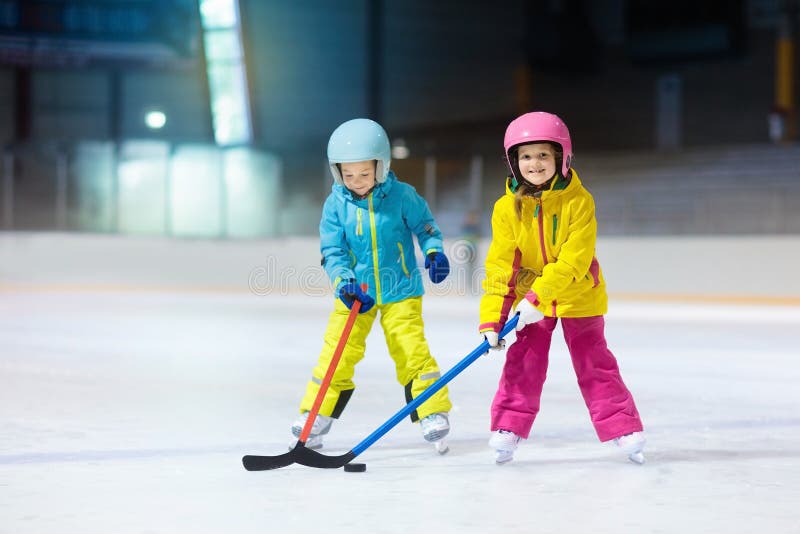 Children play ice hockey on indoor rink. Healthy winter sport for kids. Boy and girl with hockey sticks hitting puck. Child skating. Little kid on sports training after school. Snow and ice fun. Children play ice hockey on indoor rink. Healthy winter sport for kids. Boy and girl with hockey sticks hitting puck. Child skating. Little kid on sports training after school. Snow and ice fun