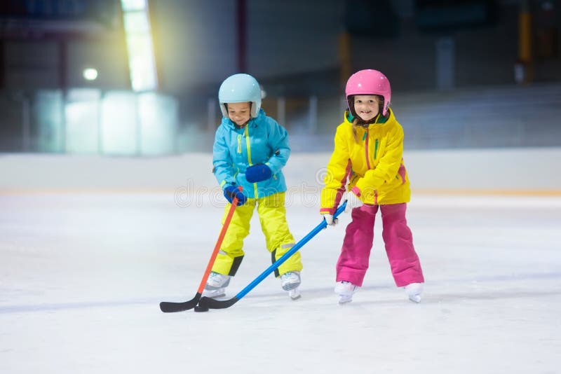 Children play ice hockey on indoor rink. Healthy winter sport for kids. Boy and girl with hockey sticks hitting puck. Child skating. Little kid on sports training after school. Snow and ice fun. Children play ice hockey on indoor rink. Healthy winter sport for kids. Boy and girl with hockey sticks hitting puck. Child skating. Little kid on sports training after school. Snow and ice fun.