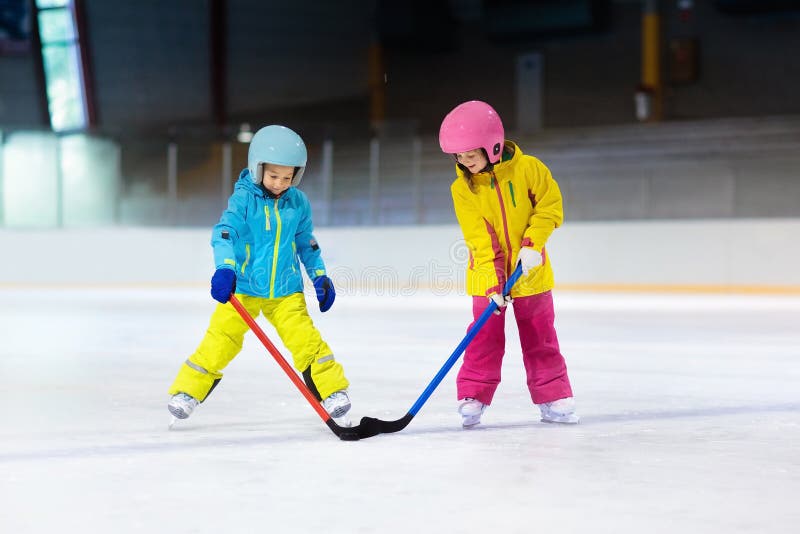 Children play ice hockey on indoor rink. Healthy winter sport for kids. Boy and girl with hockey sticks hitting puck. Child skating. Little kid on sports training after school. Snow and ice fun. Children play ice hockey on indoor rink. Healthy winter sport for kids. Boy and girl with hockey sticks hitting puck. Child skating. Little kid on sports training after school. Snow and ice fun.