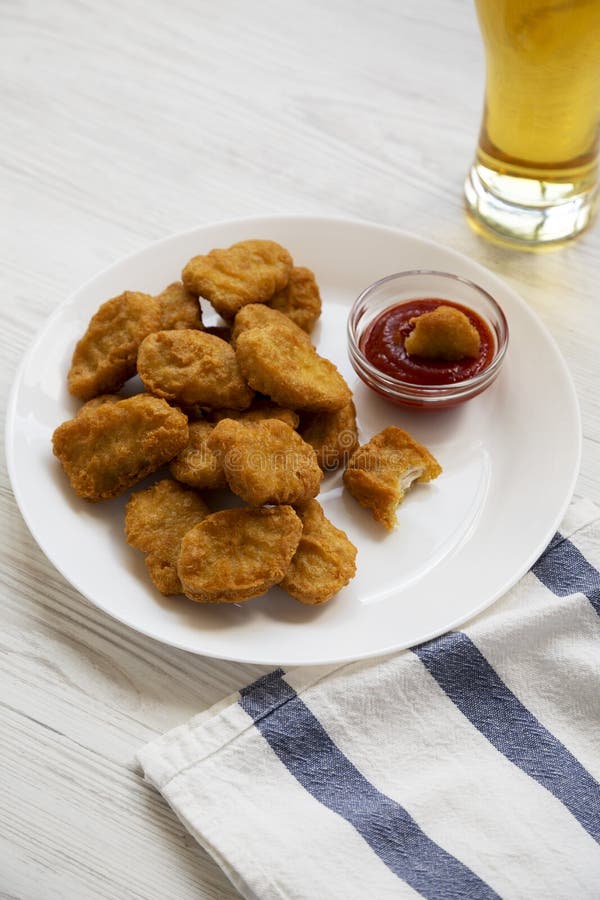 Kippengoudklompjes met ketchup en glas koud bier op een witte houten lijst, lage hoekmening royalty-vrije stock afbeelding Kippengoudklompjes met ketchup en glas koud bier op een witte houten lijst, lage hoekmening royalty-vrije stock afbeelding