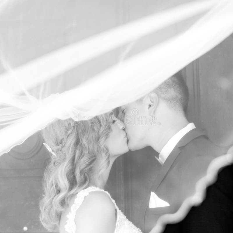 The kiss. Bride and groom kisses tenderly in the shadow of a flying veil. Artistic black and white wedding photo.