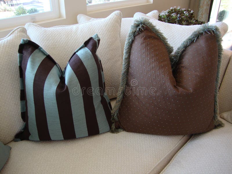 Beautiful brown and blue pillows one striped and one with dots and fringe on a cream colored sofa or couch. Beautiful brown and blue pillows one striped and one with dots and fringe on a cream colored sofa or couch
