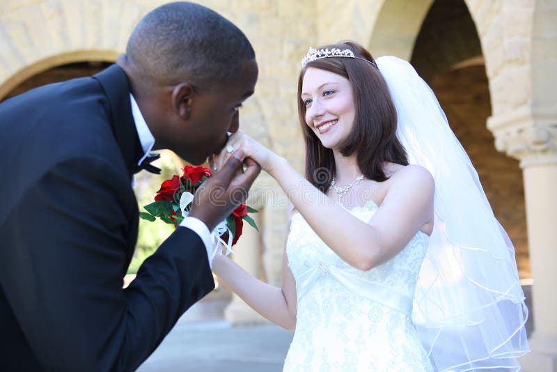 African American groom kisses the bride's hand on their wedding day. African American groom kisses the bride's hand on their wedding day.