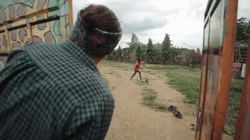 KISUMU KENJA, MAJ, - 15, 2018: Kaukaska kobieta ono przygląda się nad ogrodzeniem Afrykański chłopiec nastolatek jedzie hulajnoga