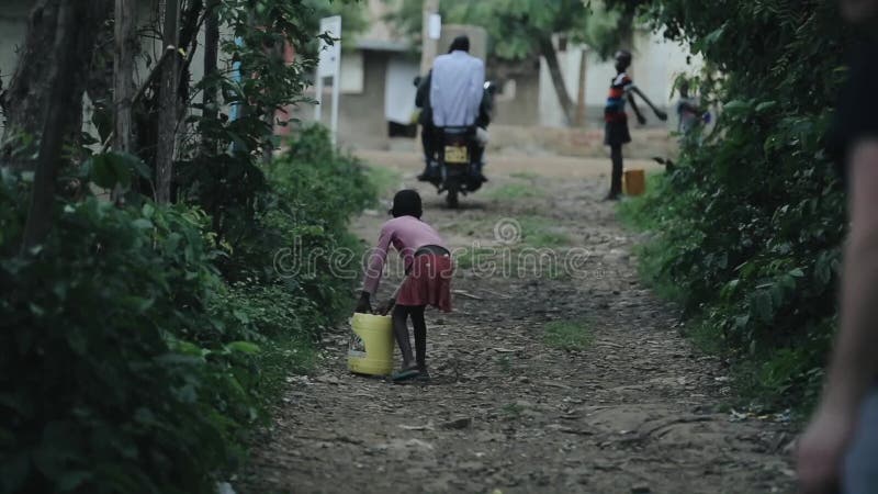 Kisumu Kenja, Maj, - 17, 2018: Tylny widok niesie kanister z wodą afrykańska dziewczyna dzieciaka odprowadzenie przez drogi
