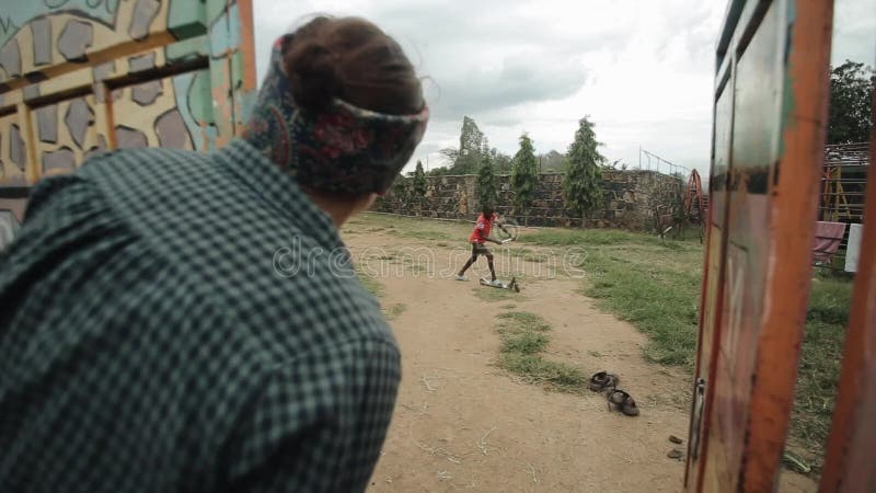 KISUMU KENYA - MAJ 15, 2018: Den Caucasian kvinnan plirar över staketet Afrikansk pojketonåring som rider en sparkcykel stock video KISUMU KENYA - MAJ 15, 2018: Den Caucasian kvinnan plirar över staketet Afrikansk pojketonåring som rider en sparkcykel stock video