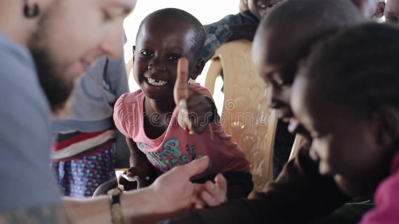 KISUMU, ΚΈΝΥΑ - 19 ΜΑΐΟΥ 2018: Ομάδα μικρών ευτυχών παιδιών από την Αφρική και καυκάσιου εθελοντή στο φτωχό χωριό απόθεμα βίντεο KISUMU, ΚΈΝΥΑ - 19 ΜΑΐΟΥ 2018: Ομάδα μικρών ευτυχών παιδιών από την Αφρική και καυκάσιου εθελοντή στο φτωχό χωριό απόθεμα βίντεο