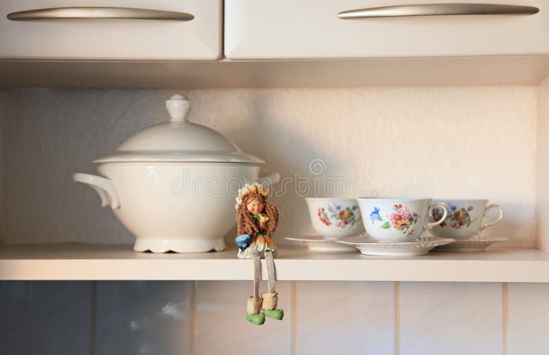 Kitchen cabinet board with a doll and cups