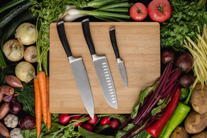 Kitchen Knives Set on Wood Cutting Board with Fresh Vegetables. Vegan Raw Food. Healthy Eating Concept stock photos