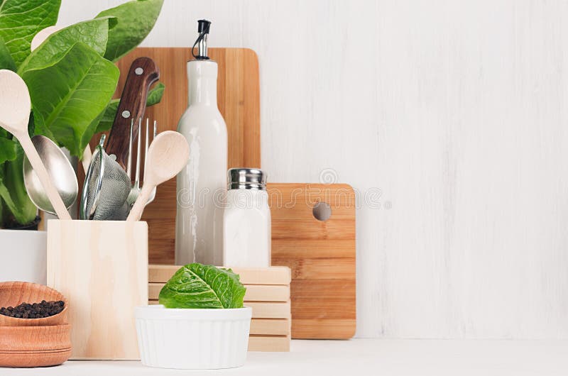 Kitchen modern decor - beige wooden utensils, brown cutting boards, green plant on soft light white wood background.
