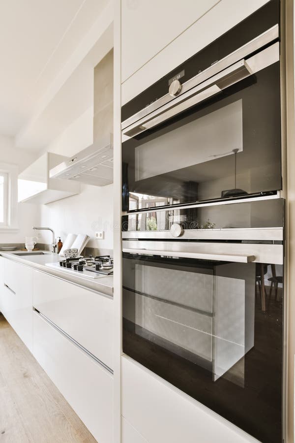 a modern kitchen with white cabinets and black oven hoods on the wall in the room is light wood flooring. a modern kitchen with white cabinets and black oven hoods on the wall in the room is light wood flooring
