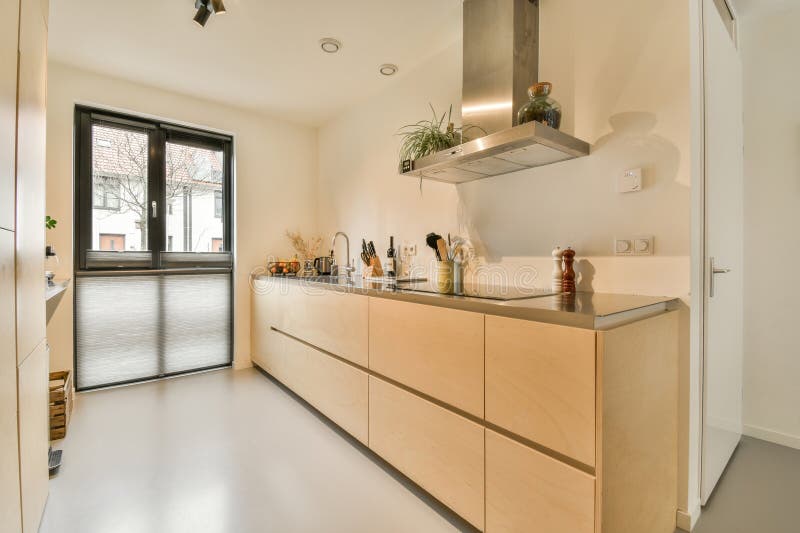 a modern kitchen with wood cabinetry and stainless steel hoods on the wall above it is an open door that leads to a. a modern kitchen with wood cabinetry and stainless steel hoods on the wall above it is an open door that leads to a