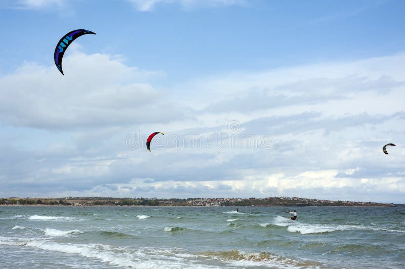 Kitesurfers ride kites on Black Sea at sandy beach in Bulgaria, Sozopol on sunny day at sunset on blue sky and clouds background. royalty free stock images Kitesurfers ride kites on Black Sea at sandy beach in Bulgaria, Sozopol on sunny day at sunset on blue sky and clouds background. royalty free stock images