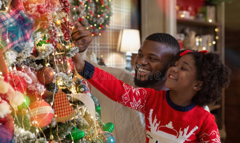 Klein afro meisje dat papa helpt om de kerstboom van de familie te versieren