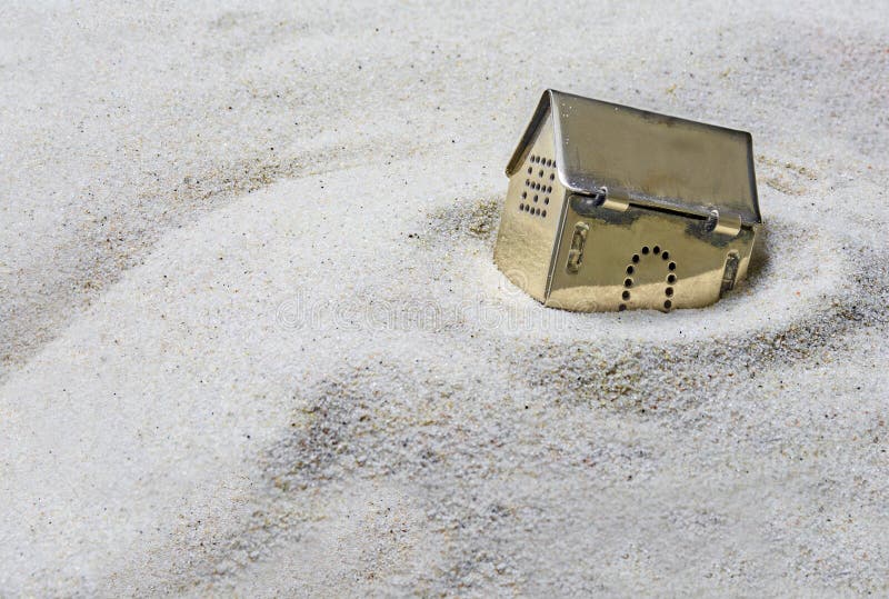 Klein gouden modelhuis die in het zand, concept dalen risico stock fotografie Klein gouden modelhuis die in het zand, concept dalen risico stock fotografie