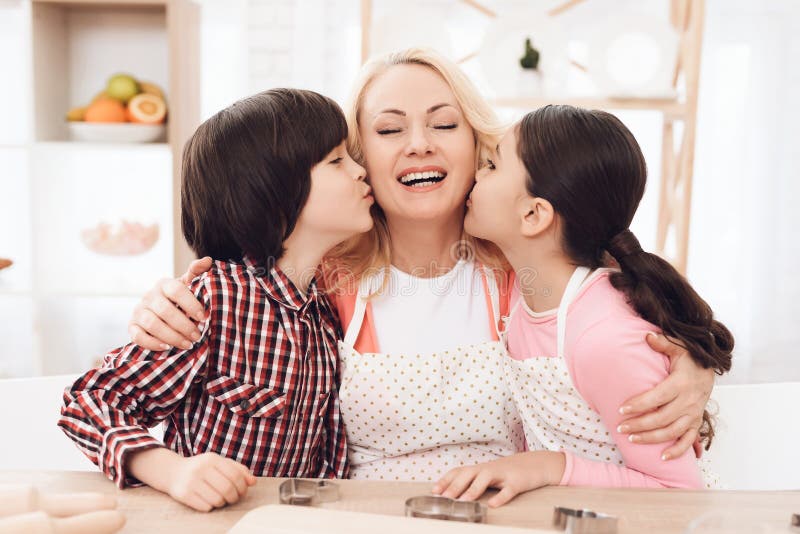 Kleine Enkelkinder küssen die schöne Großmutter, die in der Küche sitzt Schokoladenplätzchenmischung, backende Formen und Bonbon lizenzfreie stockbilder Kleine Enkelkinder küssen die schöne Großmutter, die in der Küche sitzt Schokoladenplätzchenmischung, backende Formen und Bonbon lizenzfreie stockbilder