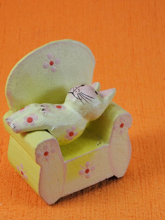Kleine gelbe hölzerne Katze, die auf einem kleinen Holzstuhl liegt stockbild Kleine gelbe hölzerne Katze, die auf einem kleinen Holzstuhl liegt stockbild