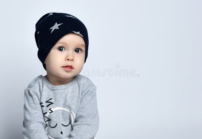 Kleine jongetje peuter in grijze, onbedachtzame springpak, kapje en barefoot op de vloer en glimlachend met opgetilde handen royalty-vrije stock afbeelding Kleine jongetje peuter in grijze, onbedachtzame springpak, kapje en barefoot op de vloer en glimlachend met opgetilde handen royalty-vrije stock afbeelding