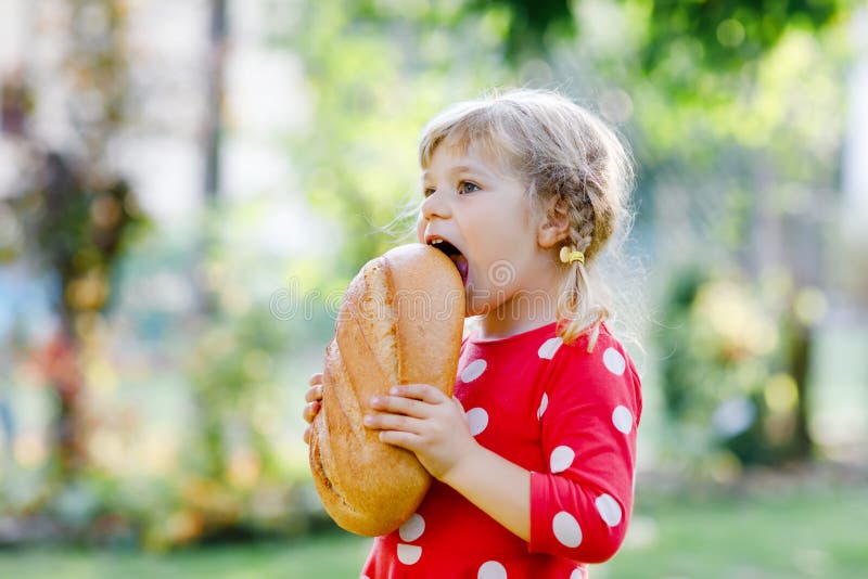 Kleine peutermeisje met een groot brood. leuk kind dat in de openlucht gezond brood eet. hongerig kind.