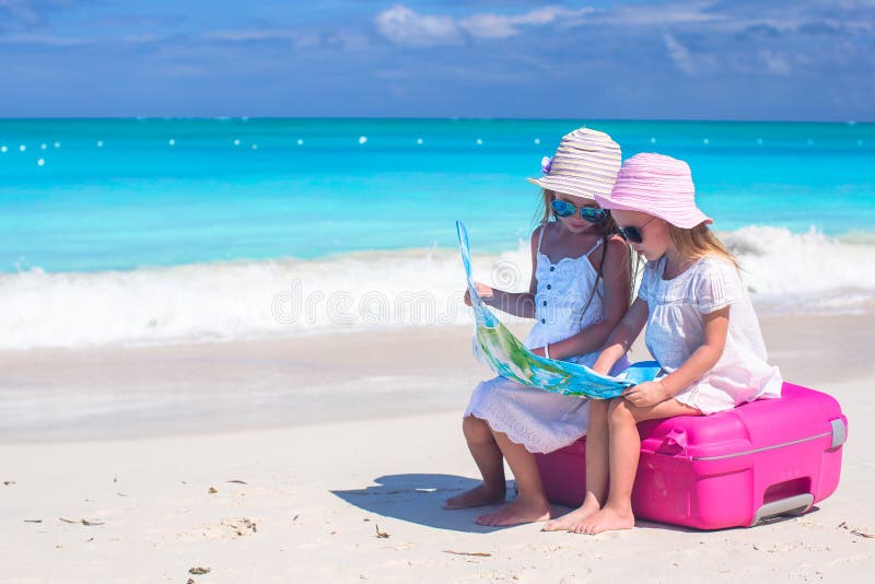 Kleine reizende Mädchen, die auf großem Koffer und einer Karte am tropischen Strand sitzen lizenzfreies stockbild Kleine reizende Mädchen, die auf großem Koffer und einer Karte am tropischen Strand sitzen lizenzfreies stockbild