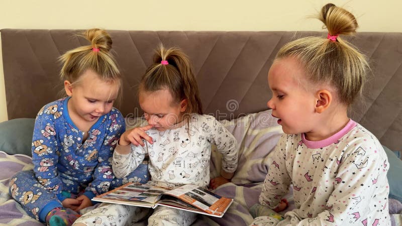 Kleine Schwestern lesen zusammen ein Buch, während sie auf dem Bett sitzen. sie tragen Schlafanzug