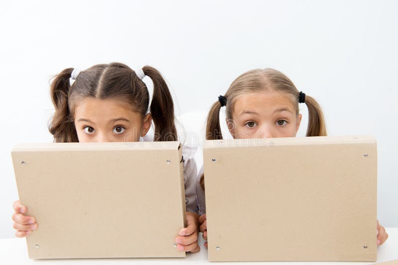 Kleine ungeschickte Mädchen verstecken Gesichter hinter Dateiordnern Kleine ungeschickte Mädchen genießen, zusammen zu spielen