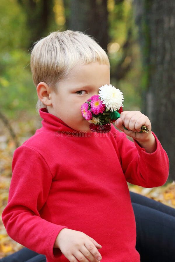 Kleiner blonder Junge im Rot schnüffelt Blumen stockfotografie Kleiner blonder Junge im Rot schnüffelt Blumen stockfotografie