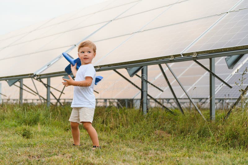 Kleiner glücklicher Junge spielt mit Spielzeugflugzeug in der Nähe von Sonnenkollektoren. stockbild