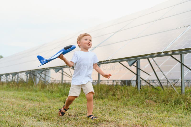 Kleiner glücklicher Junge spielt mit Spielzeugflugzeug in der Nähe von Sonnenkollektoren. lizenzfreies stockfoto