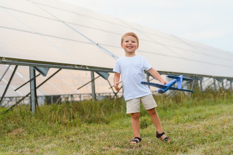 Kleiner glücklicher Junge spielt mit Spielzeugflugzeug in der Nähe von Sonnenkollektoren. lizenzfreies stockfoto