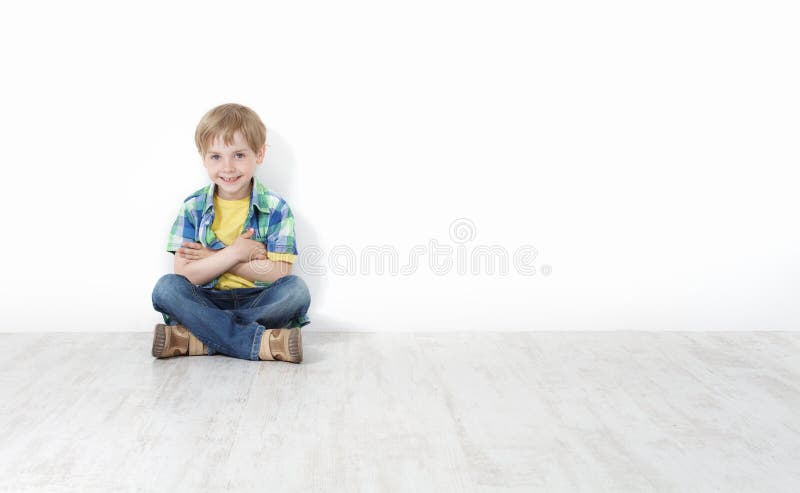 Kleiner Junge, der auf dem Fußboden sich lehnt an der Wand sitzt