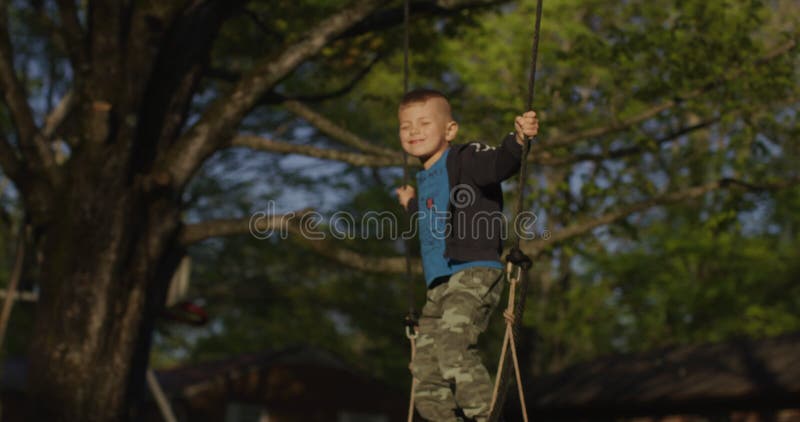 Kleiner Junge, der ein Schwankungen in einem grünen Park mit Füßen tritt. glückliche Kindheit. stock footage