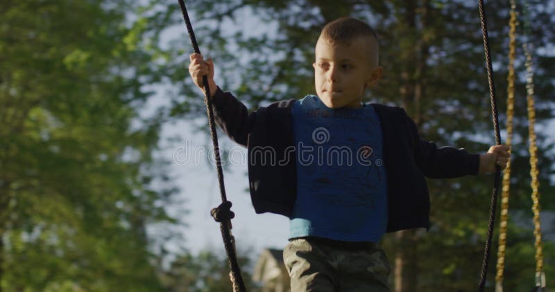 Kleiner Junge, der ein Schwankungen in einem grünen Park mit Füßen tritt. glückliche Kindheit. stock footage