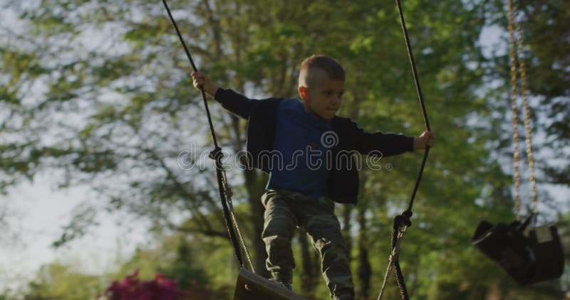 Kleiner Junge, der ein Schwankungen in einem grünen Park mit Füßen tritt. glückliche Kindheit. stock video