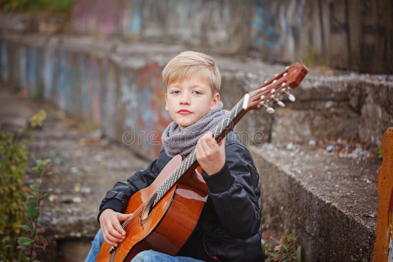 Kleiner Junge, der Gitarre am Herbstkältetag spielt Children& x27; s-intere stockbilder Kleiner Junge, der Gitarre am Herbstkältetag spielt Children& x27; s-intere stockbilder