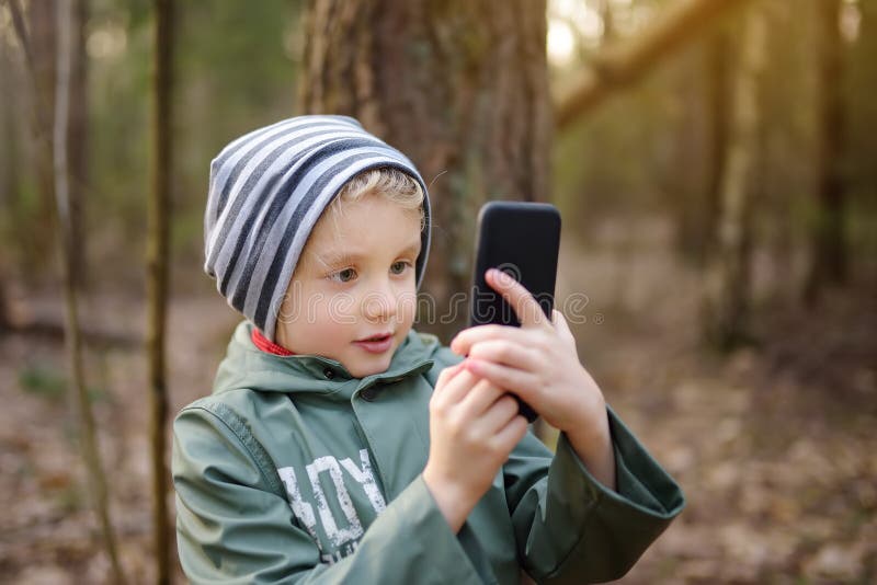 Kleiner Junge, der im Frühjahr oder Herbst beim Spaziergang im Wald Foto- oder Videoanruf mit Smartphone anruft stockbild Kleiner Junge, der im Frühjahr oder Herbst beim Spaziergang im Wald Foto- oder Videoanruf mit Smartphone anruft stockbild