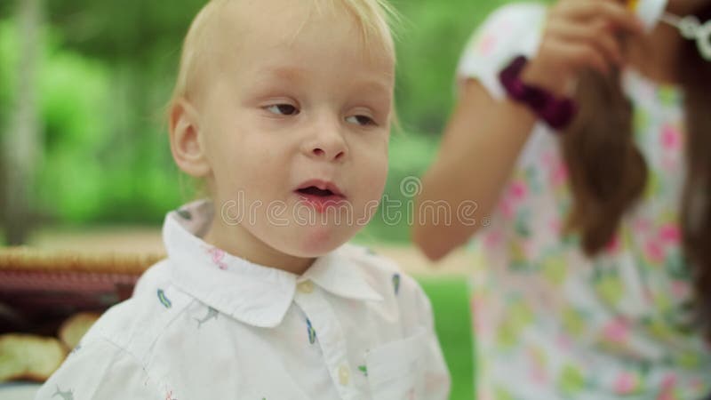 Kleiner Junge, der Kirsche am Picknick im Wald essen. Schlagseifenblasen des Mädchens an der Kamera