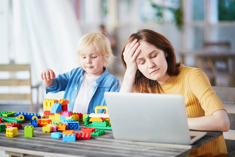 Kleiner Junge, der mit Baublöcken während seine Mutter arbeitet an Computer spielt