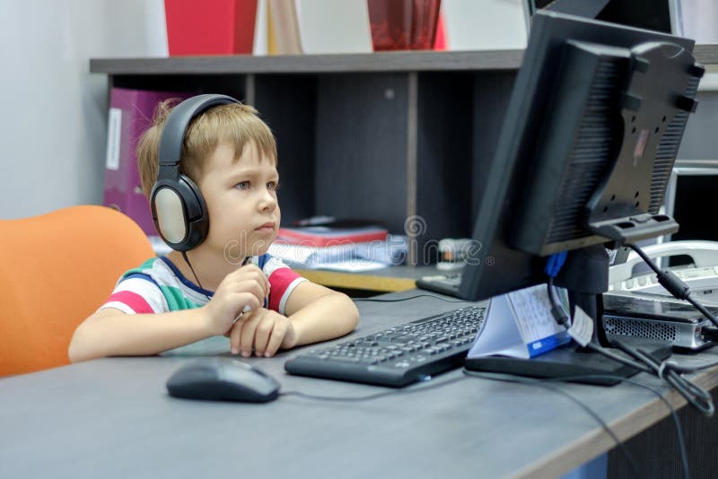 Kleiner Junge mit den Kopfhörern, die am Computer im Büro sitzen stockfotos Kleiner Junge mit den Kopfhörern, die am Computer im Büro sitzen stockfotos