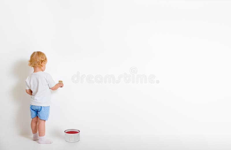 Kleiner Junge mit der Pinsel- und Blechdose, die zurück nahe weißer Wand steht lizenzfreies stockfoto