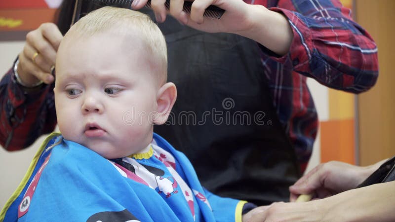 Kleiner Junge Schneidet Den Friseur Er Sitzt In Einem Stuhl Der Wie Ein Auto Aussieht Mutter Die Es Mit Ihm Ablenkt Und Spielt Stock Footage Video Von Schneidet Mutter