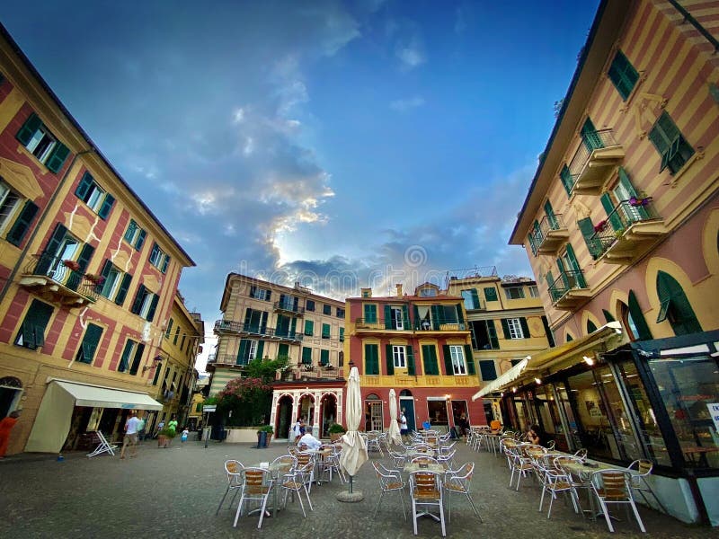 Wide view of a small plaza in Liguria, Italy, Celle Ligure town, with chairs and tables in the dehors of the bars and restaurants, with some scattered client in distance. Wide view of a small plaza in Liguria, Italy, Celle Ligure town, with chairs and tables in the dehors of the bars and restaurants, with some scattered client in distance.