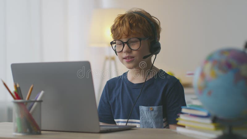 Kleiner rothaariger Junge trägt Headset mit Mikrofon Video Chat mit Tutor Blick auf Laptop und sprechen mit Lehrer stock video