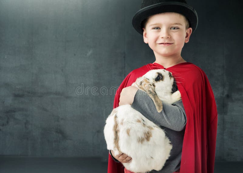 Kleiner Zauberkünstler, der ein magisches Kaninchen hält stockfotografie Kleiner Zauberkünstler, der ein magisches Kaninchen hält stockfotografie