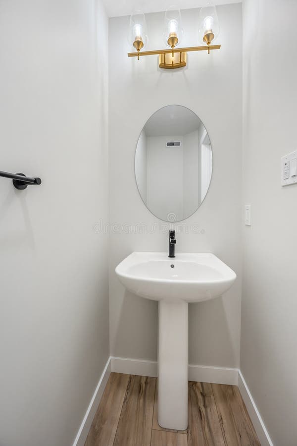 Kleines Badezimmer mit weißem Waschbecken und vergoldeter Leuchte darüber stockfoto