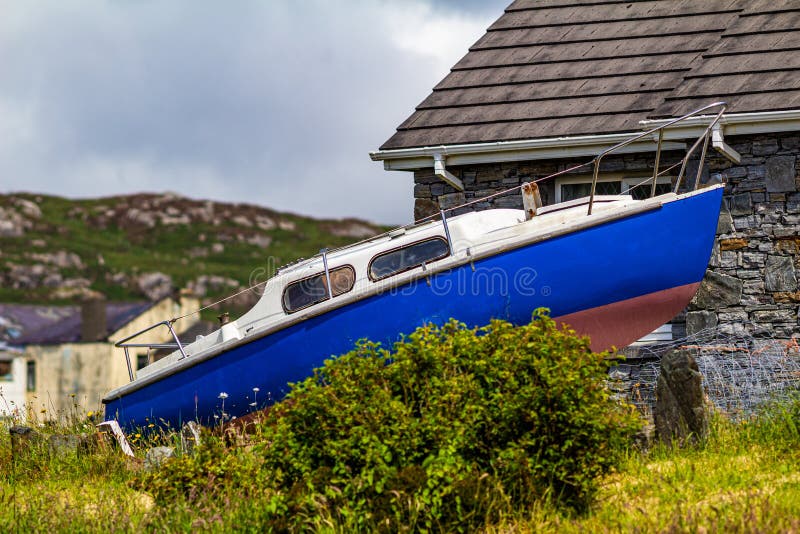 Kleines Boot neben einem Haus in der Nähe des Hafens von Clifden mit einem Berg im Hintergrund stockfoto Kleines Boot neben einem Haus in der Nähe des Hafens von Clifden mit einem Berg im Hintergrund stockfoto