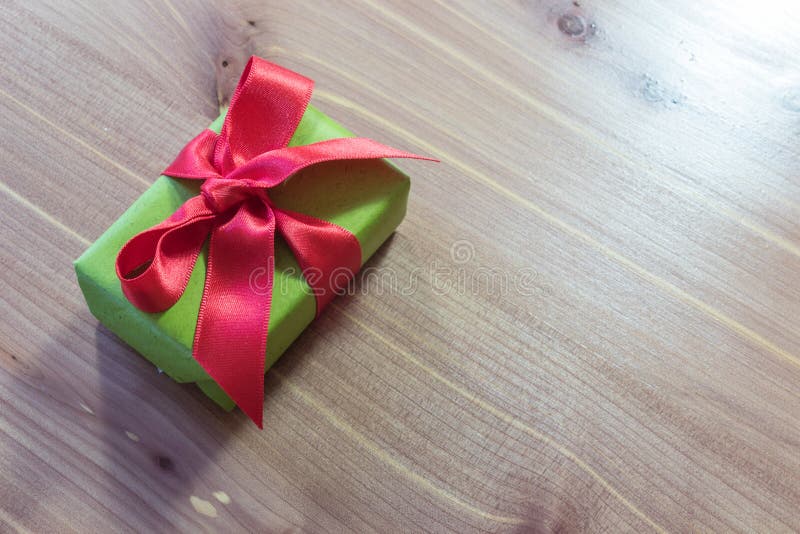 Kleines Geschenk, diagonal auf einer hölzernen Tabelle, eingewickelt im Grün mit großem rotem Satinbogen lizenzfreie stockfotos Kleines Geschenk, diagonal auf einer hölzernen Tabelle, eingewickelt im Grün mit großem rotem Satinbogen lizenzfreie stockfotos