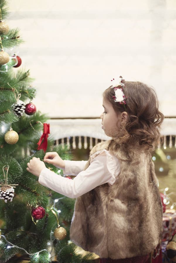 Kleines Kindermädchen, das zu Hause Weihnachtsbaum mit Bällen, zuhause verziert Abschluss oben Weihnachtsniederlassung und -glock lizenzfreie stockfotografie Kleines Kindermädchen, das zu Hause Weihnachtsbaum mit Bällen, zuhause verziert Abschluss oben Weihnachtsniederlassung und -glock lizenzfreie stockfotografie